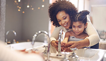 Mother helping her child wash her hands.