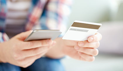 Person holding credit card and using smartphone.